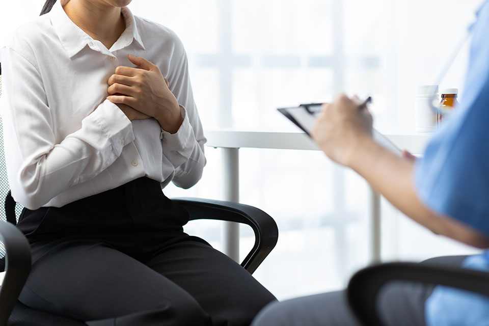 A female patient clutching her chest while attended to by a medical professional